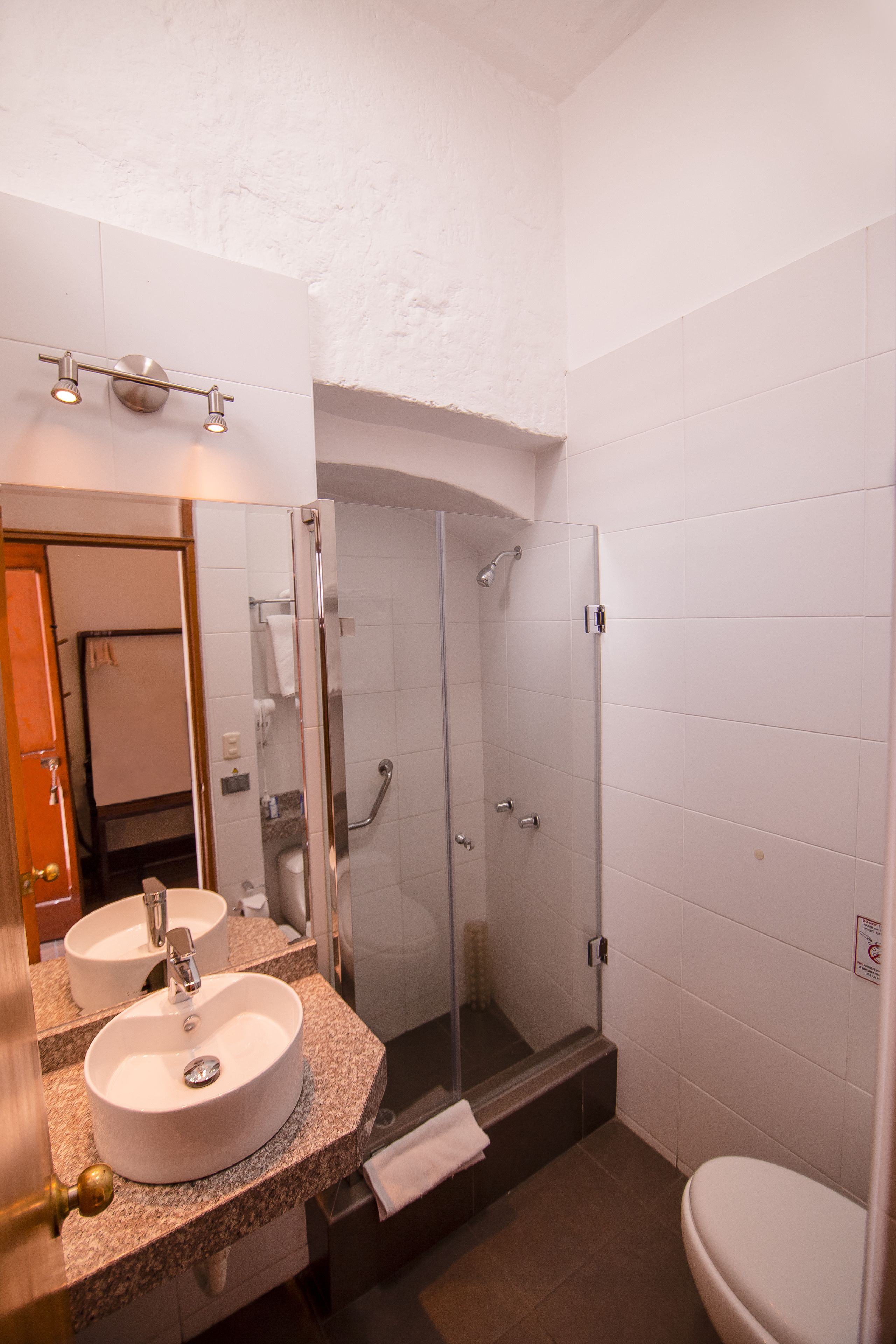 A bathroom with a double sink, a glass shower enclosure, and a toilet.