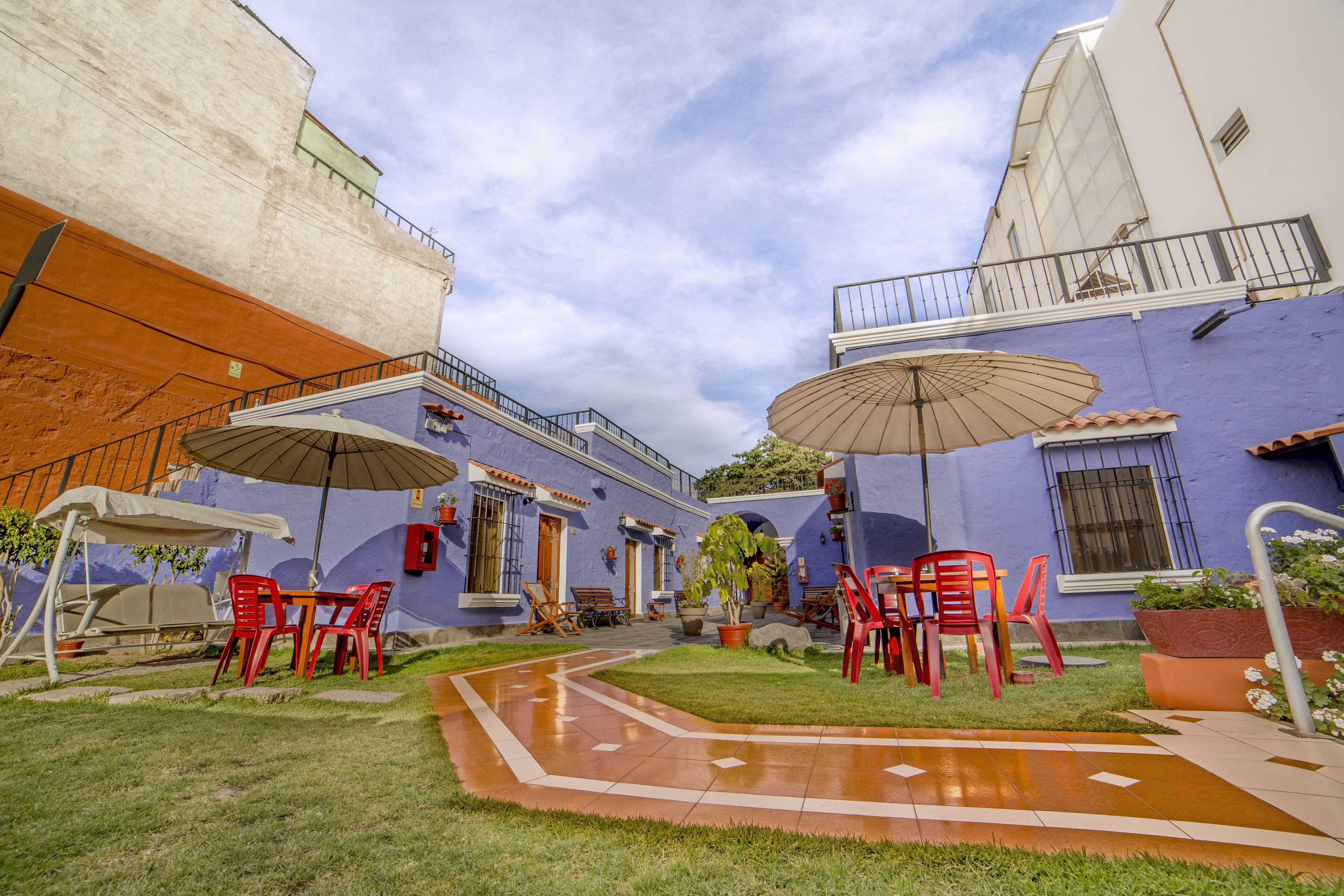 Un patio al aire libre con sillas y mesas de plástico rojo, sombrillas y un pequeño jardín.