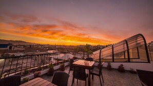 A rooftop terrace with a table and chairs, potted plants, and a view of the sunset over a cityscape. - Las Torres de Ugarte (Arequipa)