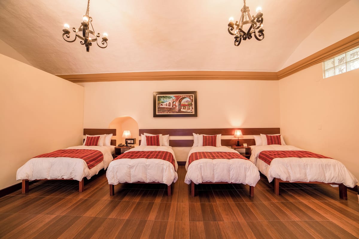 A hotel room with four single beds, wooden flooring, and two chandeliers.