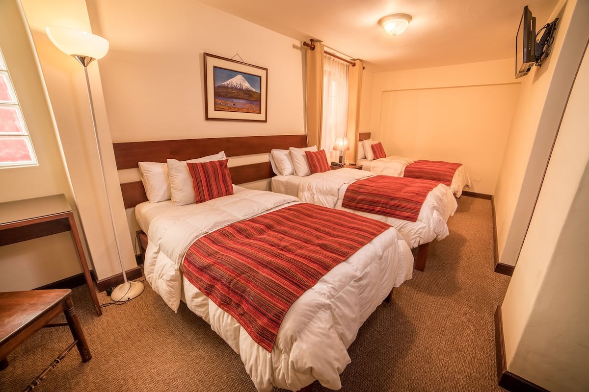 A hotel room with three beds, a desk, and a lamp.