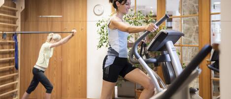 A gym with two people exercising on treadmills, wooden walls, a clock, and a potted plant.
