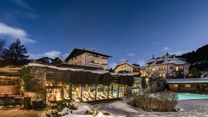 Un espacio exterior cubierto de nieve con piscina, sillones de descanso y un edificio con fachada de vidrio.