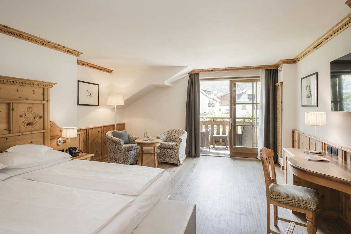 Habitación de hotel con una cama grande, un escritorio, una silla, una mesita y un balcón con vistas al exterior.