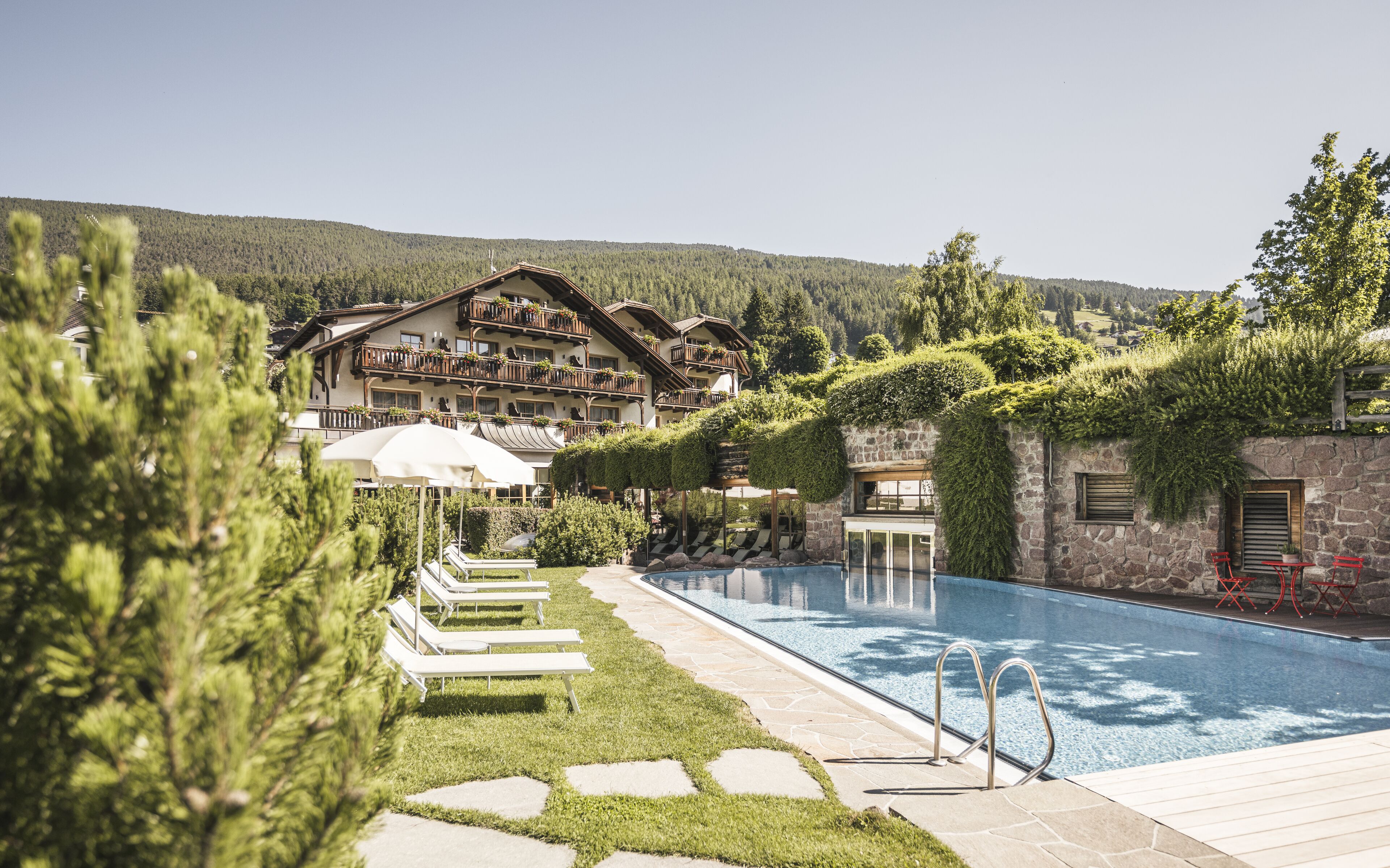 Un hôtel doté d’une piscine, de chaises longues et offrant une vue sur un paysage montagneux.