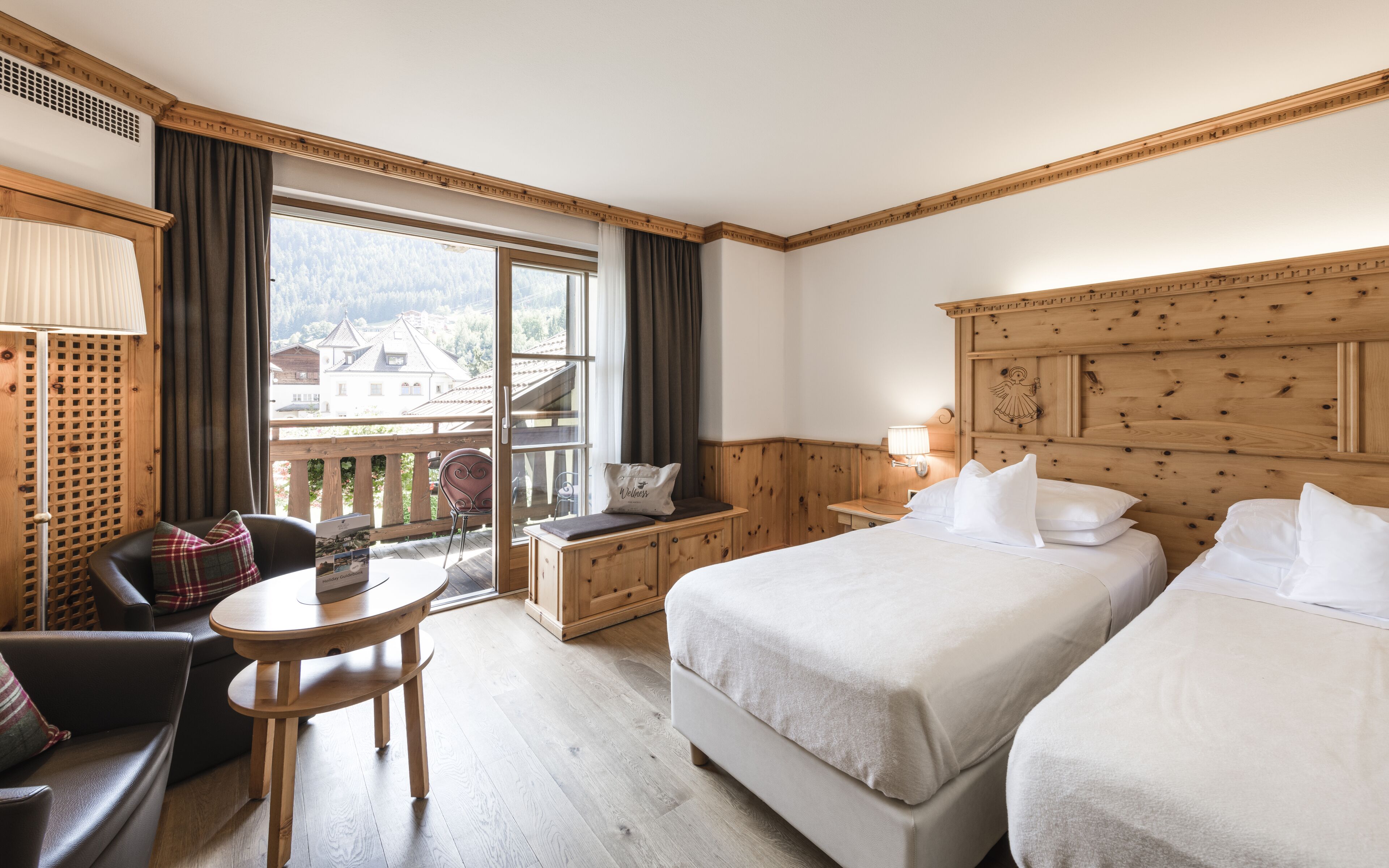 Une chambre d’hôtel avec un balcon, un bureau, deux lits et une vue sur la montagne.