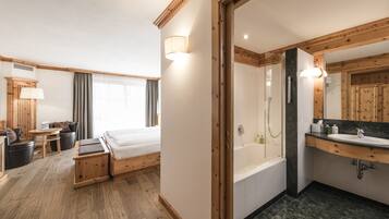 Ein Hotelzimmer mit Bett, einer Sitzecke mit Tisch und Stühlen, einem Badezimmer mit Badewanne und Waschbecken sowie Holzvertäfelung.