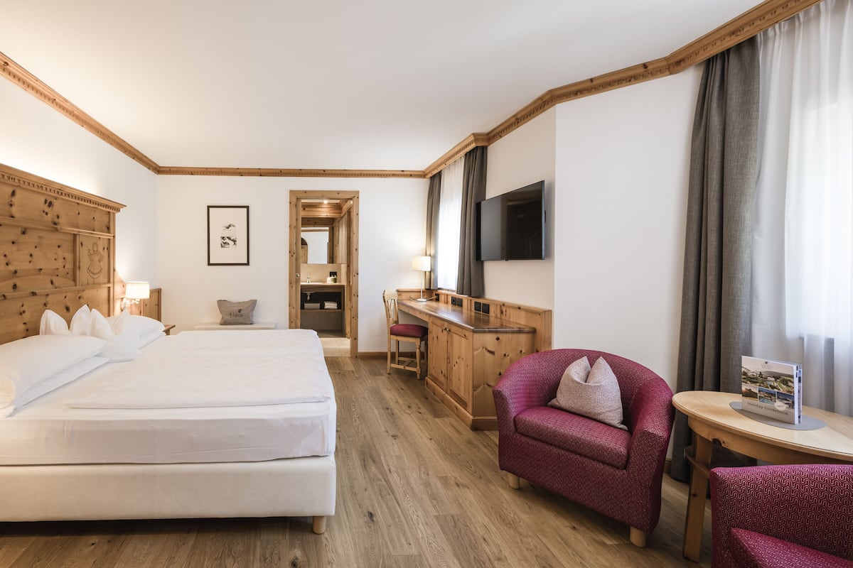 Habitación de hotel con cama, escritorio, silla, televisor y una mesita con un libro.
