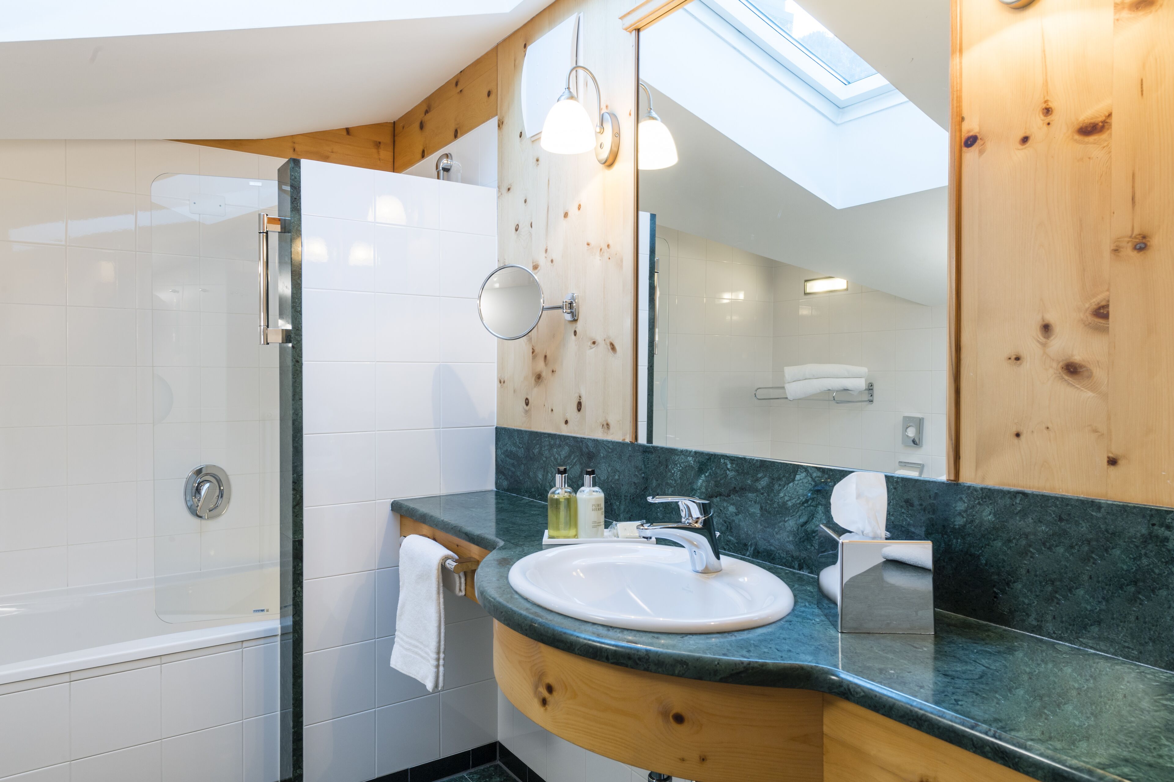 A modern bathroom with a glass-enclosed shower, a wooden vanity with a sink, and a skylight above.