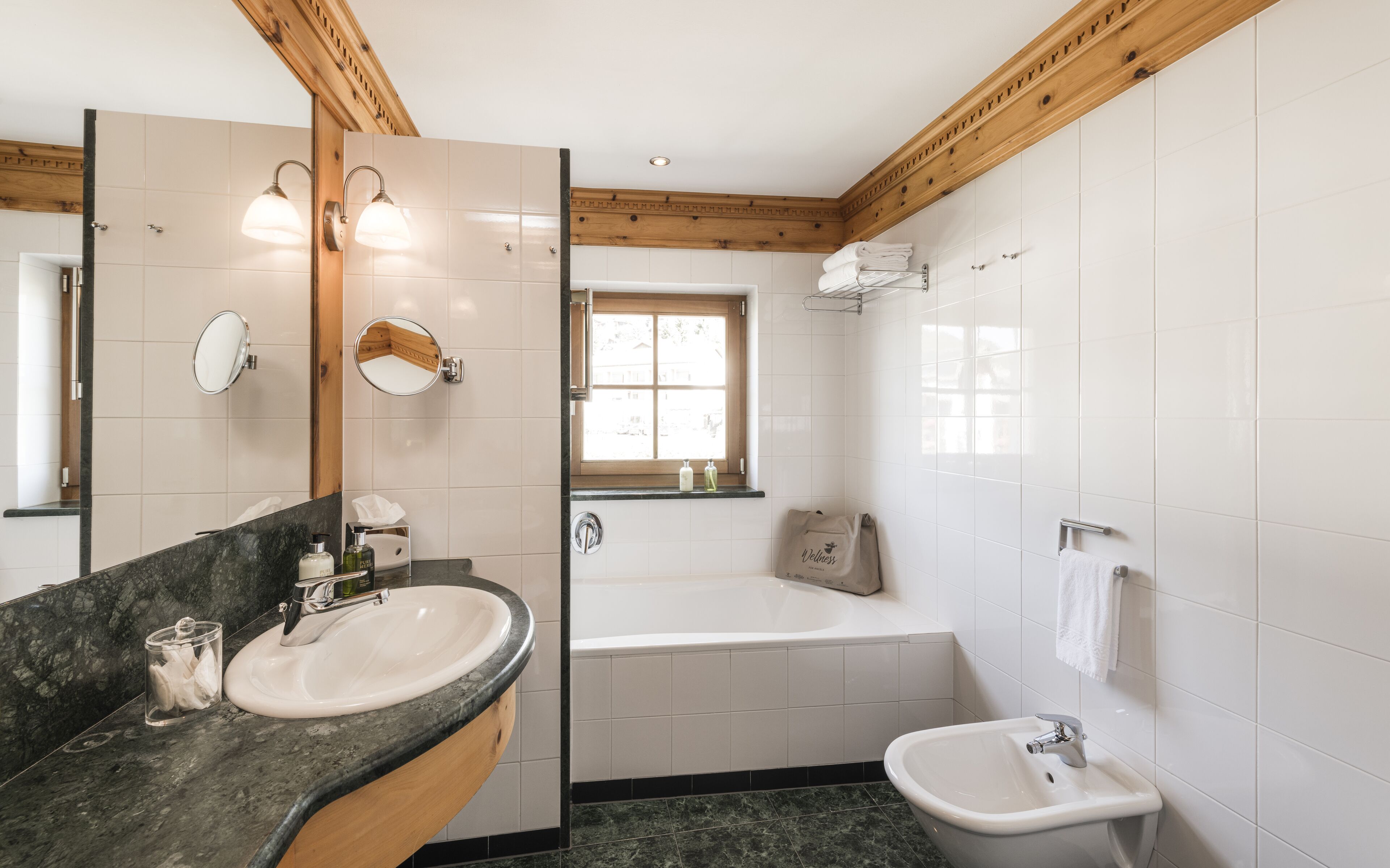 Une salle de bain dotée d’un meuble-lavabo en marbre, d’une baignoire, d’un lavabo séparé et d’une fenêtre laissant entrer la lumière naturelle.