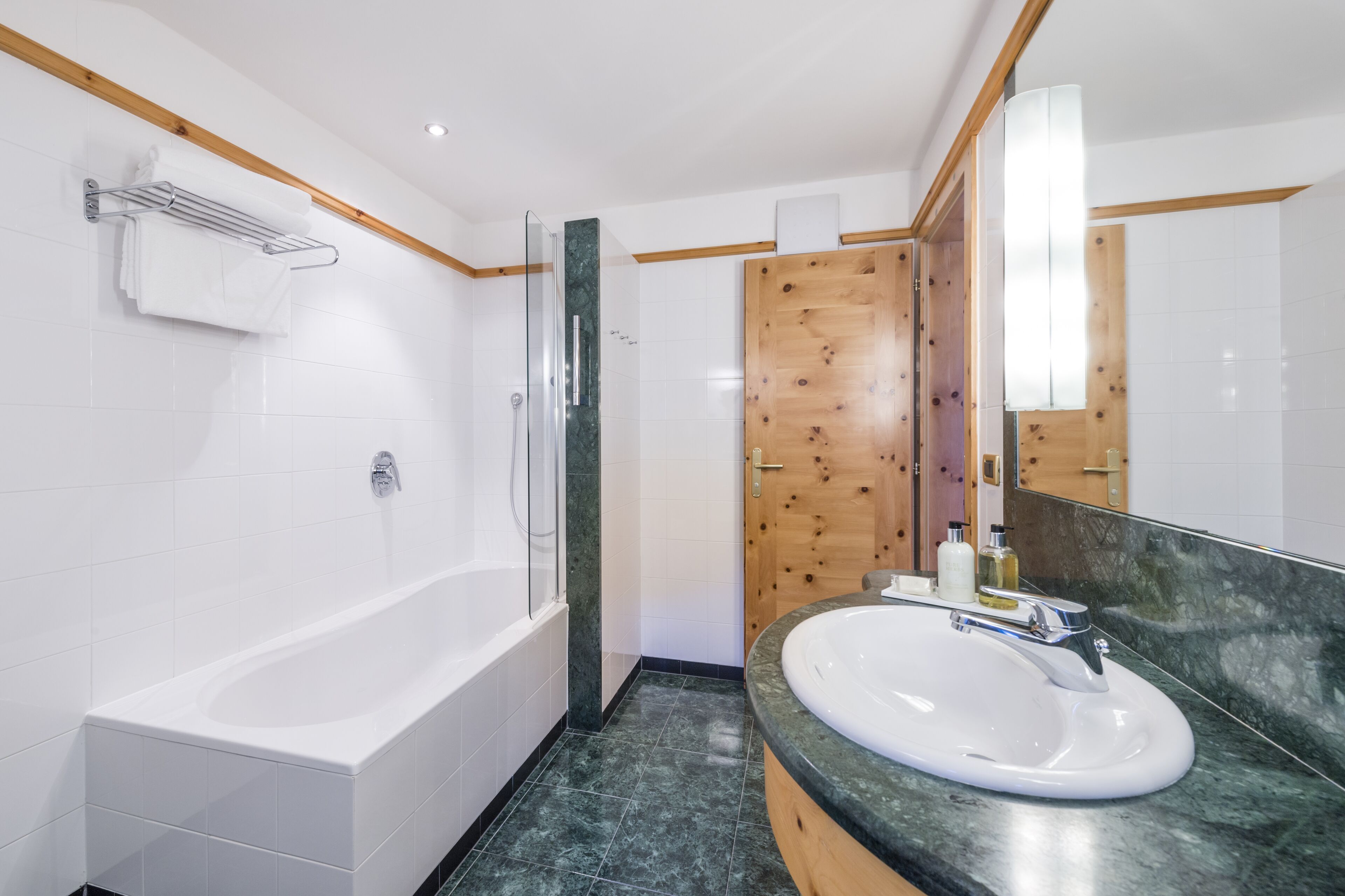 Ein modernes Badezimmer mit einer weißen Badewanne, einem Waschbecken mit Marmorplatte und einer Holztür.