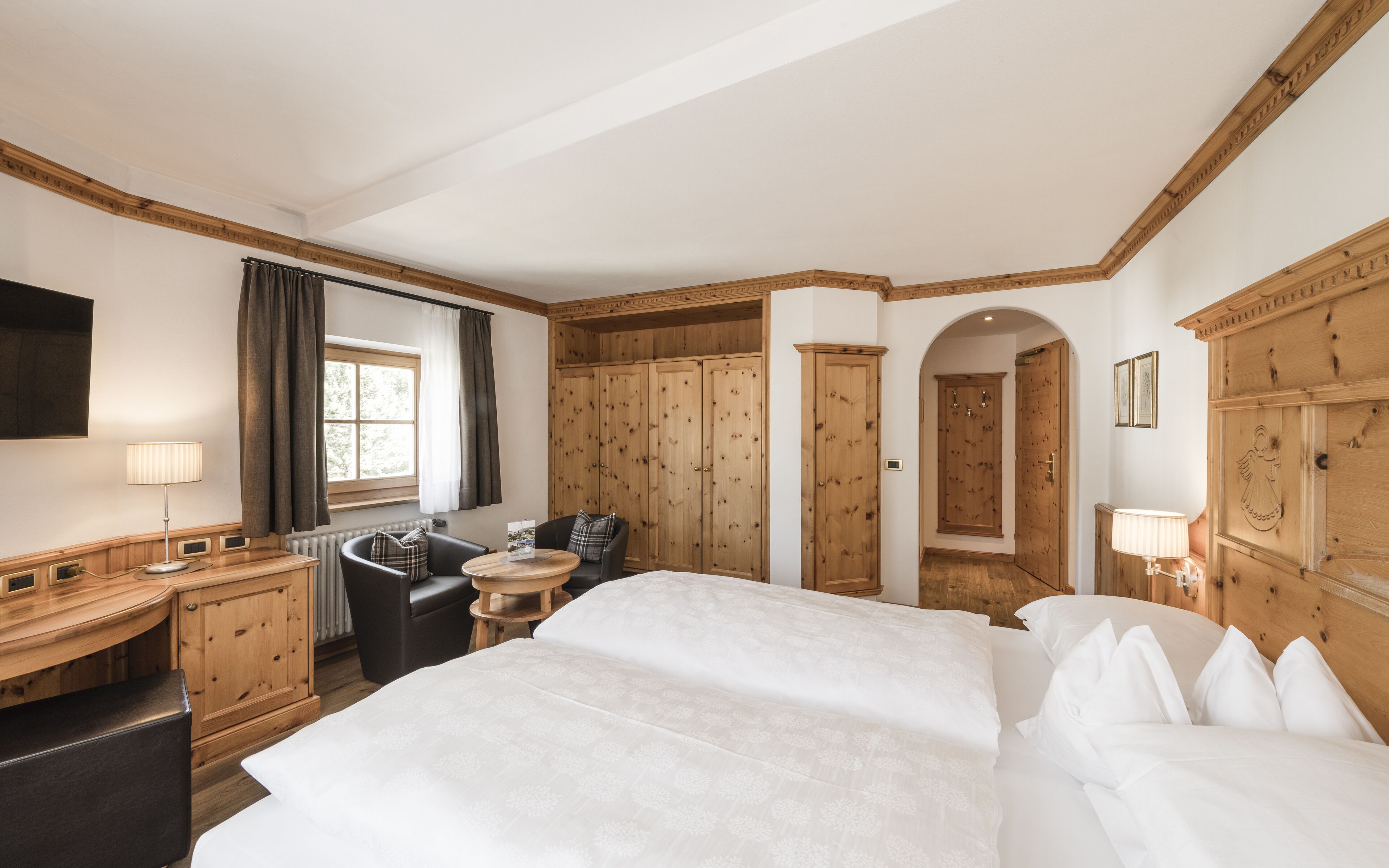 Habitación de hotel con una cama grande, un escritorio con lámpara, una silla, una mesita y armarios de madera.