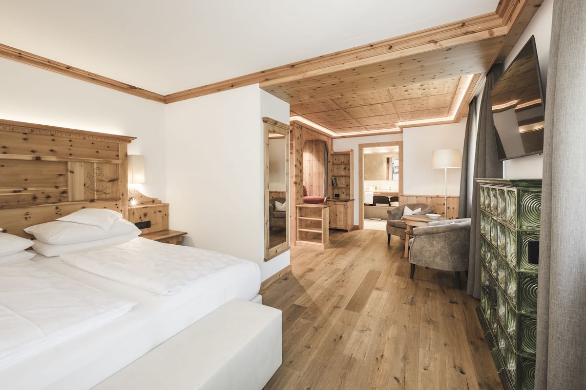 Habitación de hotel con una cama grande, cabecero de madera, un escritorio con silla, un espejo y un armario verde.