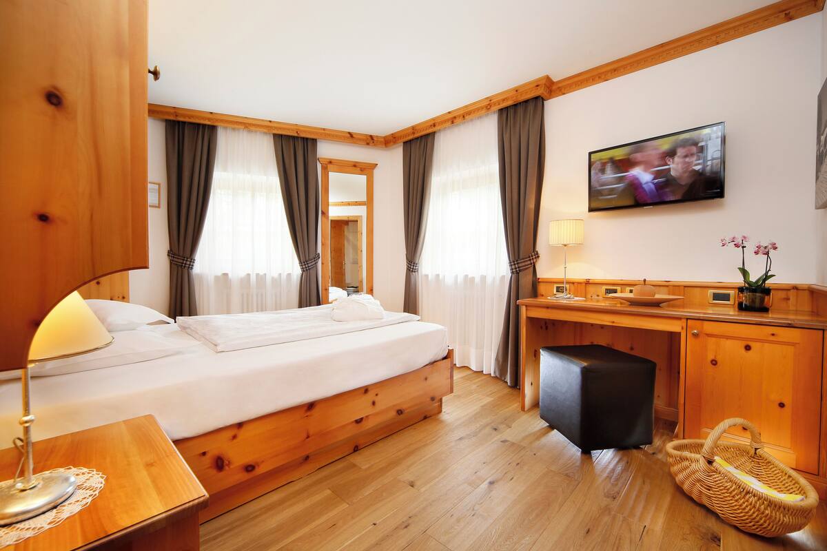 Una habitación de hotel con una cama de madera, un escritorio, un televisor y una ventana con cortinas.