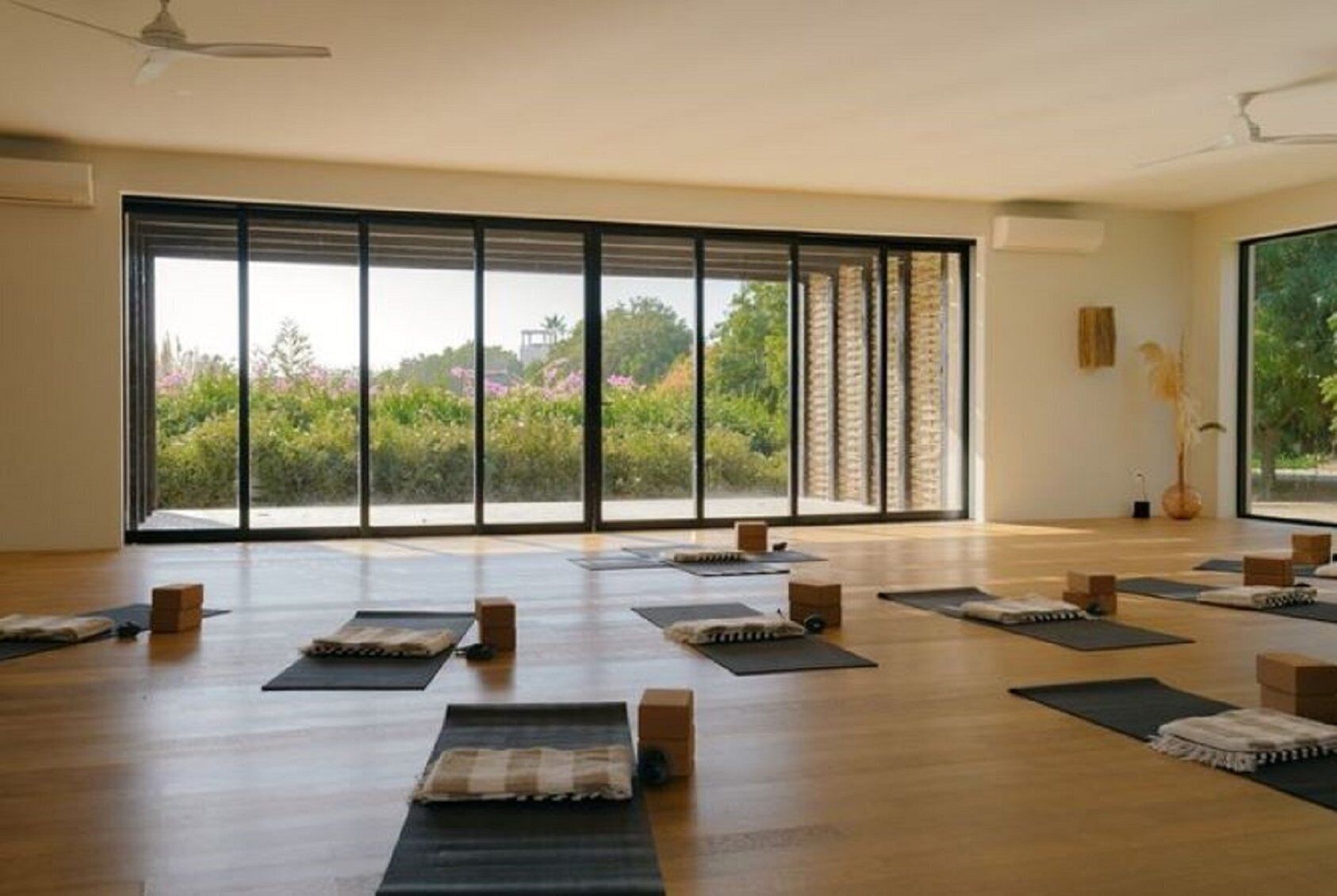 A spacious room with large windows, yoga mats, and wooden blocks arranged for a yoga session.