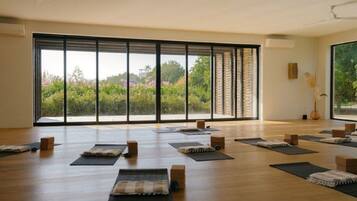 Una habitación amplia con ventanas grandes, tapetes de yoga y bloques de madera dispuestos para una sesión de yoga.