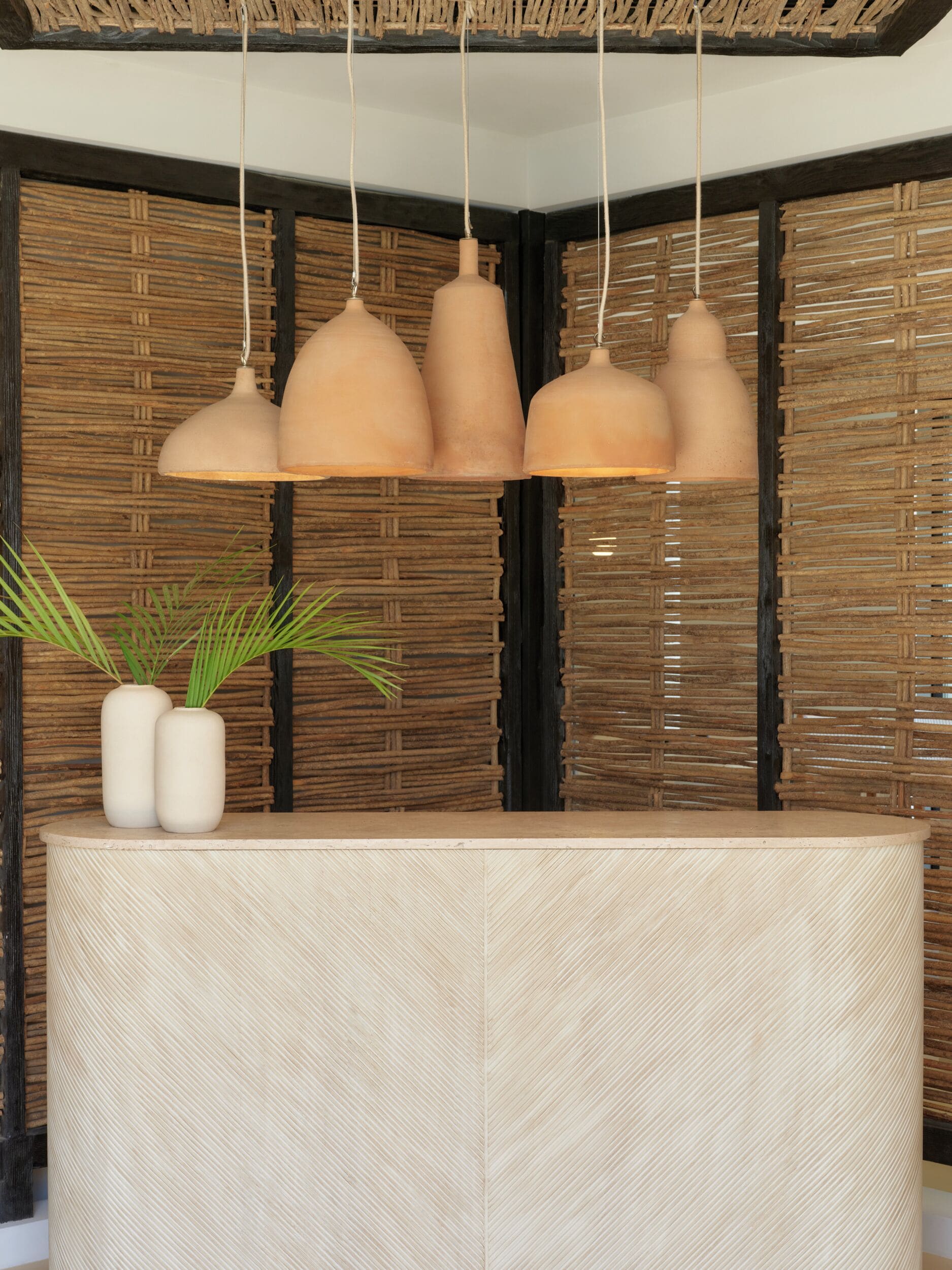 Balcão de recepção com painel de parede trançado e iluminação pendente.