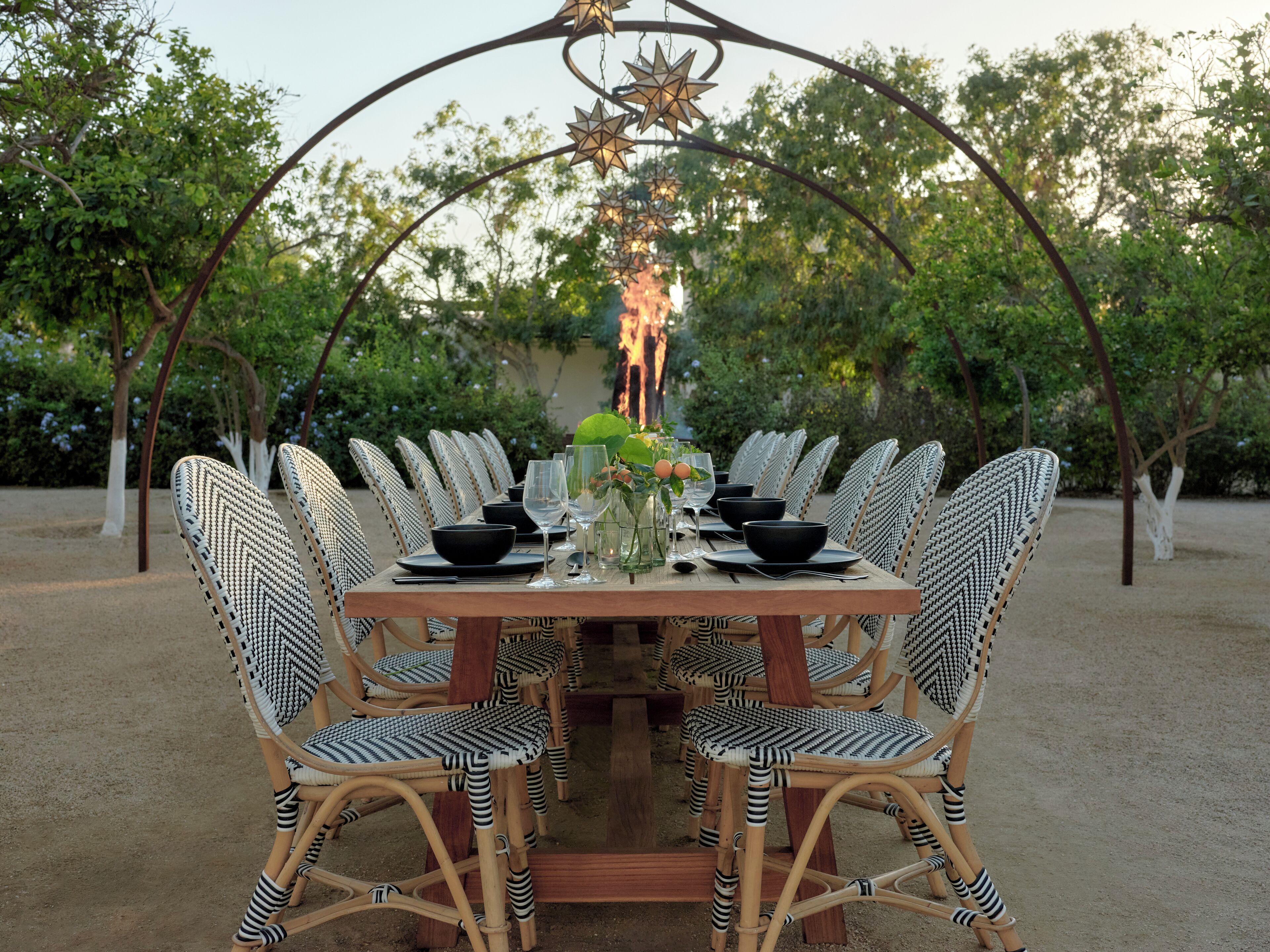A dining table set with black bowls, wine glasses, and a vase with flowers, surrounded by wicker chairs.