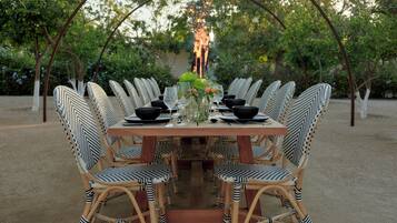 A dining table set with black bowls, wine glasses, and a vase with flowers, surrounded by wicker chairs.