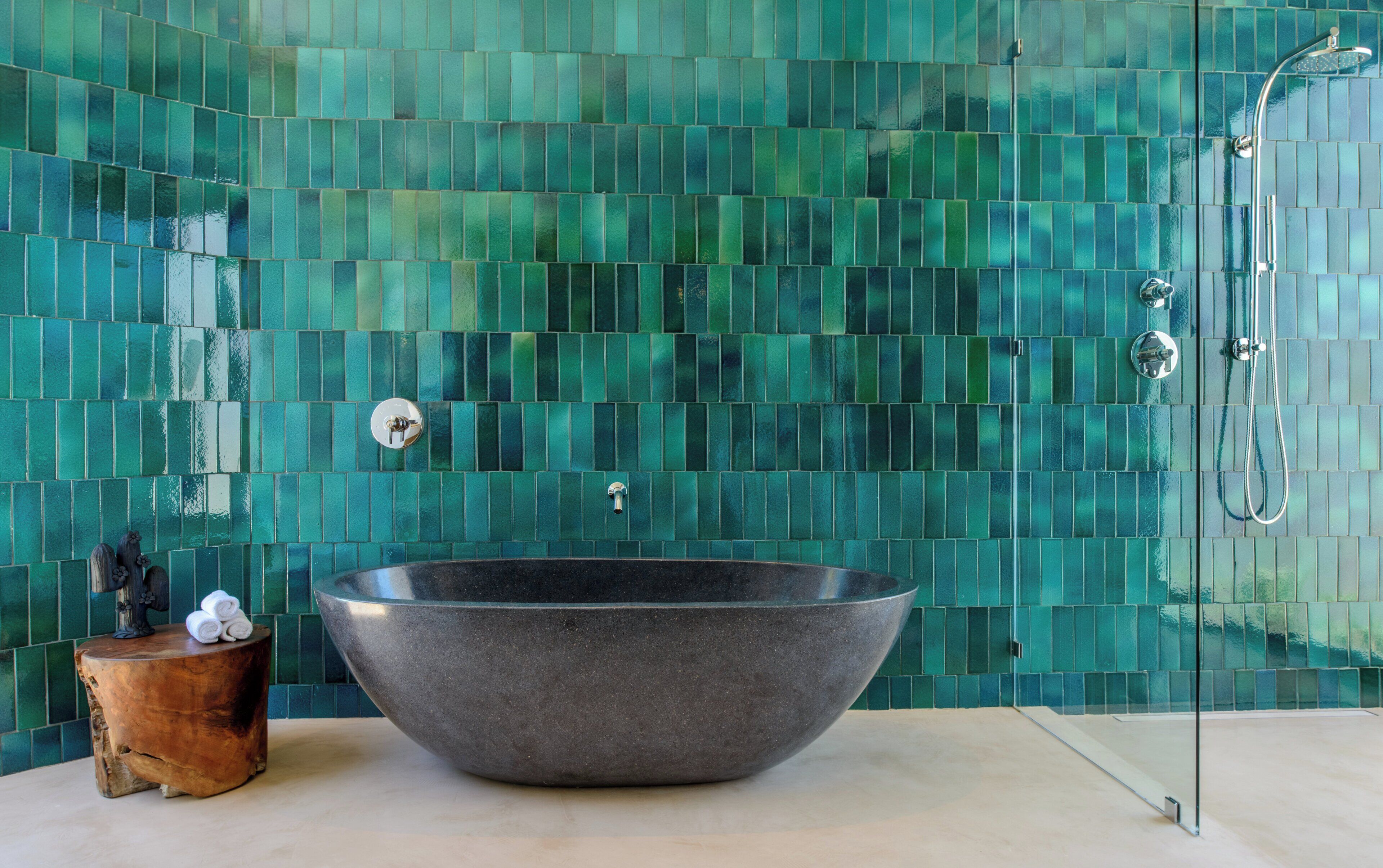 A bathroom with a large, dark-colored basin, a shower, and a wall with green mosaic tiles.