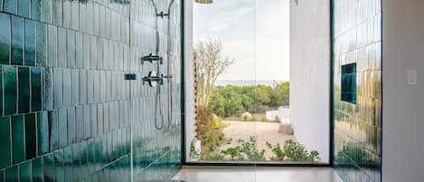 A modern bathroom with a glass shower enclosure, a bathtub, and a view of a natural landscape.