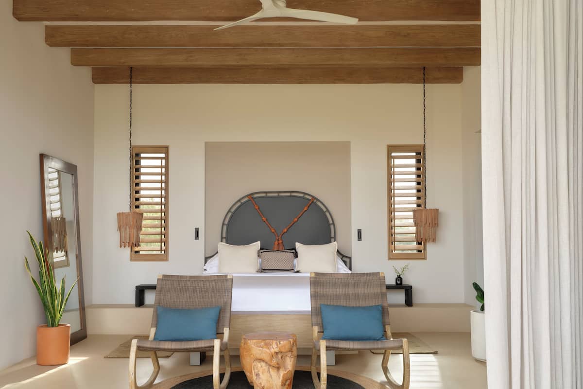 A bedroom with a bed, two chairs, a small table, and a large mirror.