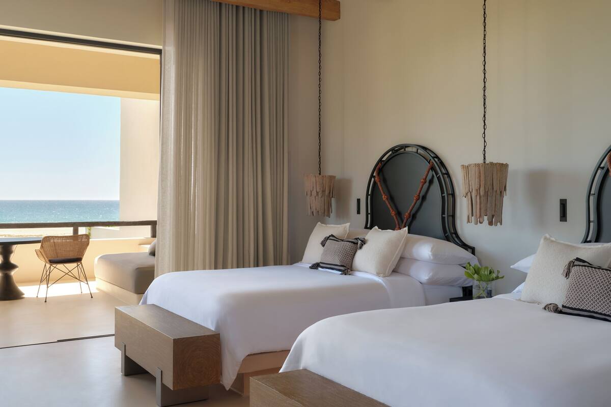 A hotel room with two beds, a large window with a view of the sea, and a hanging light fixture.