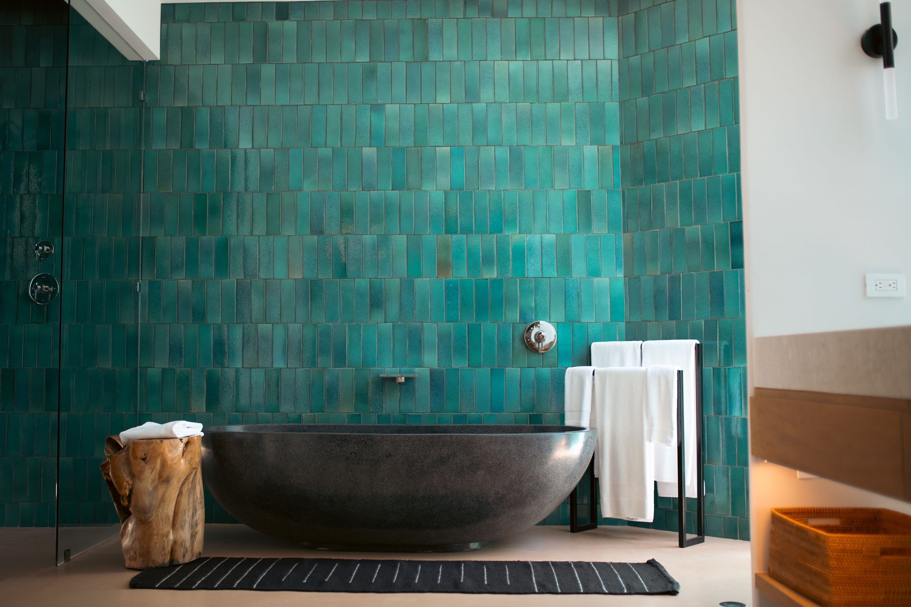 A modern bathroom with a freestanding bathtub, a wooden stool, and a tiled wall.