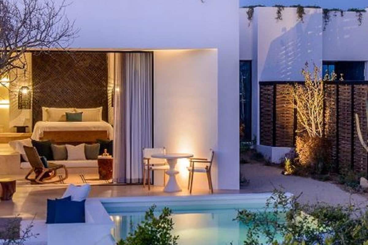 A modern hotel room with a bed, a seating area with a table and chairs, and a pool in the foreground.