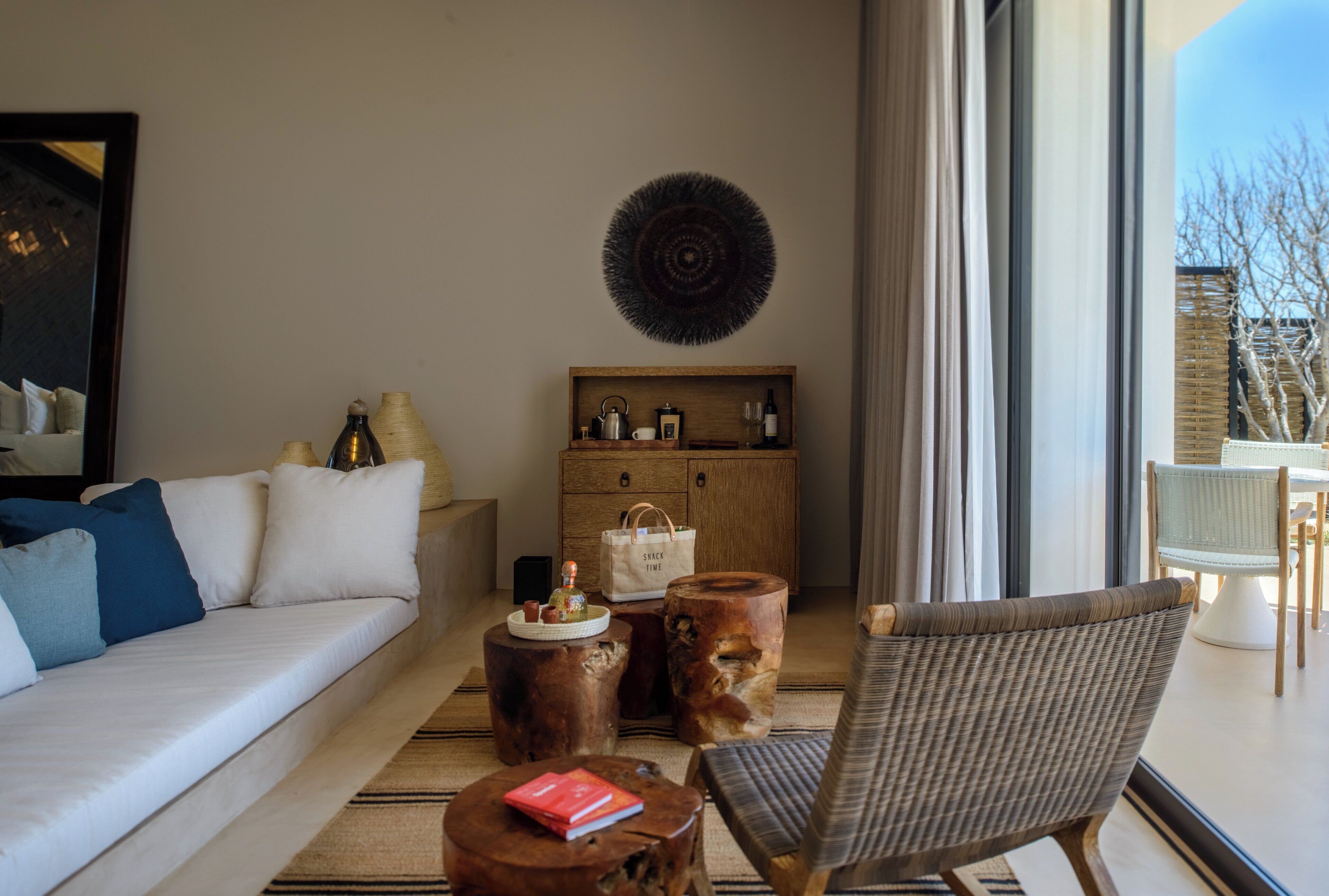 Un salon moderne comprenant un canapé, une table basse et un fauteuil, ainsi qu’un meuble en bois et une grande fenêtre donnant sur la forêt.