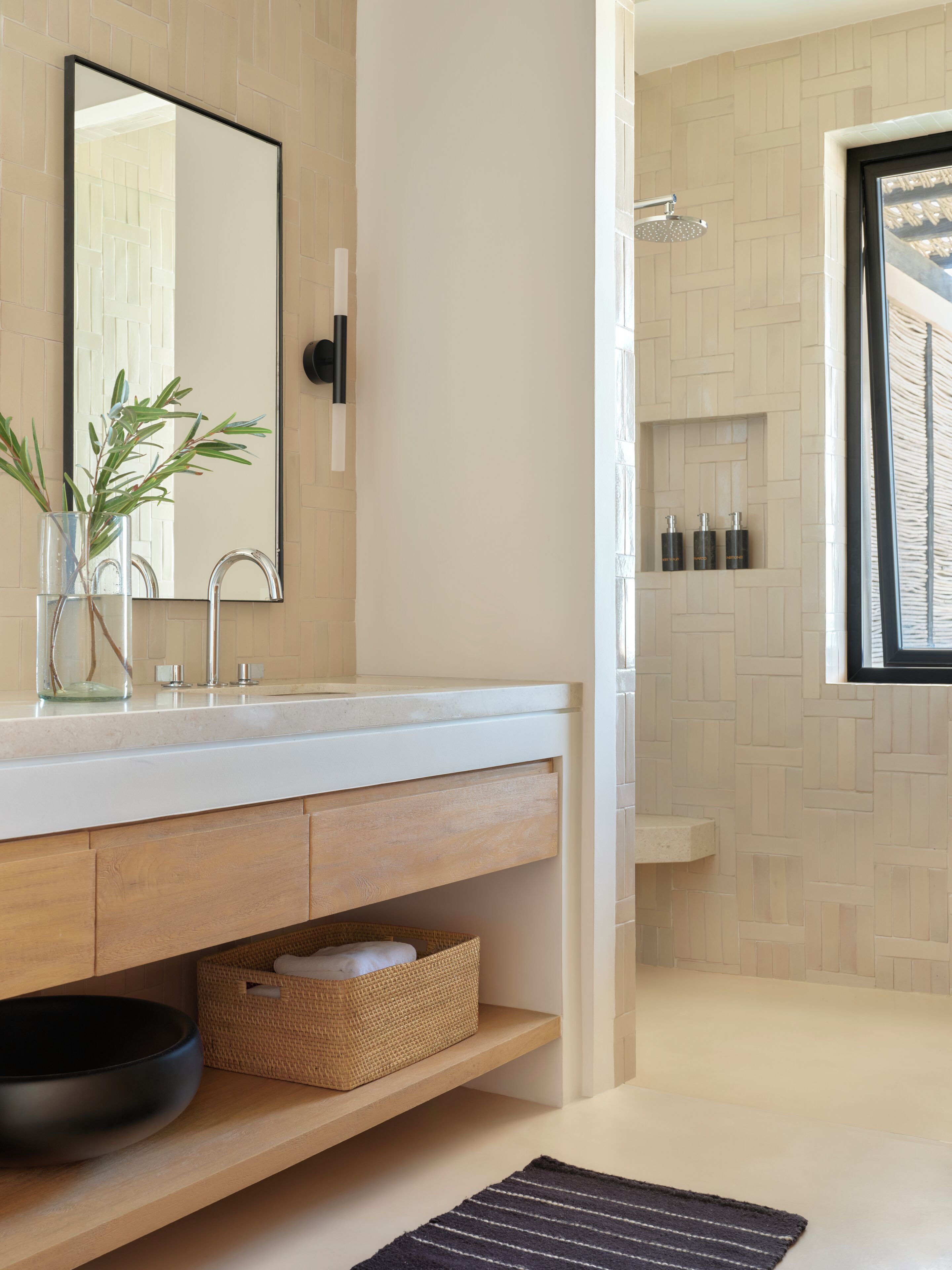 A modern bathroom with a large mirror, a sink, a shower, and a window.