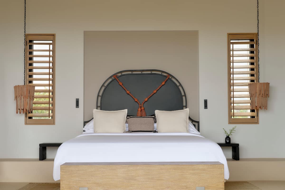 A modern bedroom with a large bed, wooden headboard, and two hanging wooden blinds.