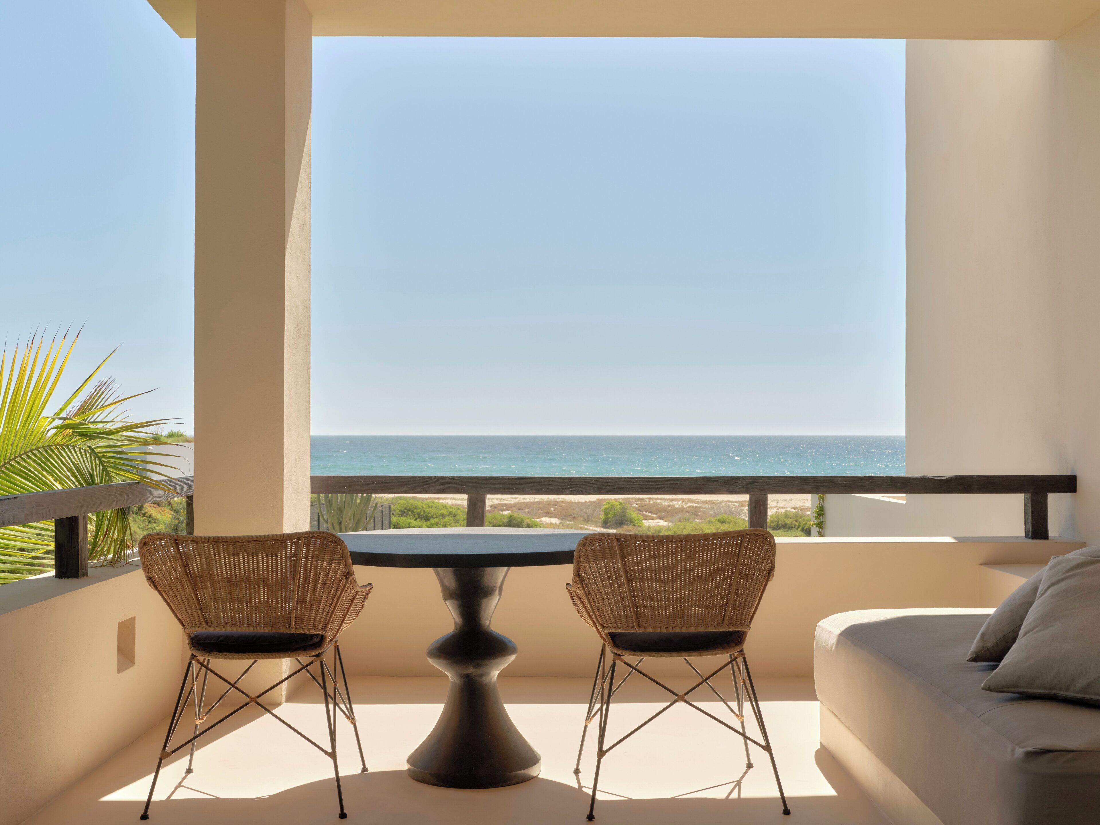 Ein Balkon mit Tisch und zwei Stühlen mit Blick auf einen Strand.