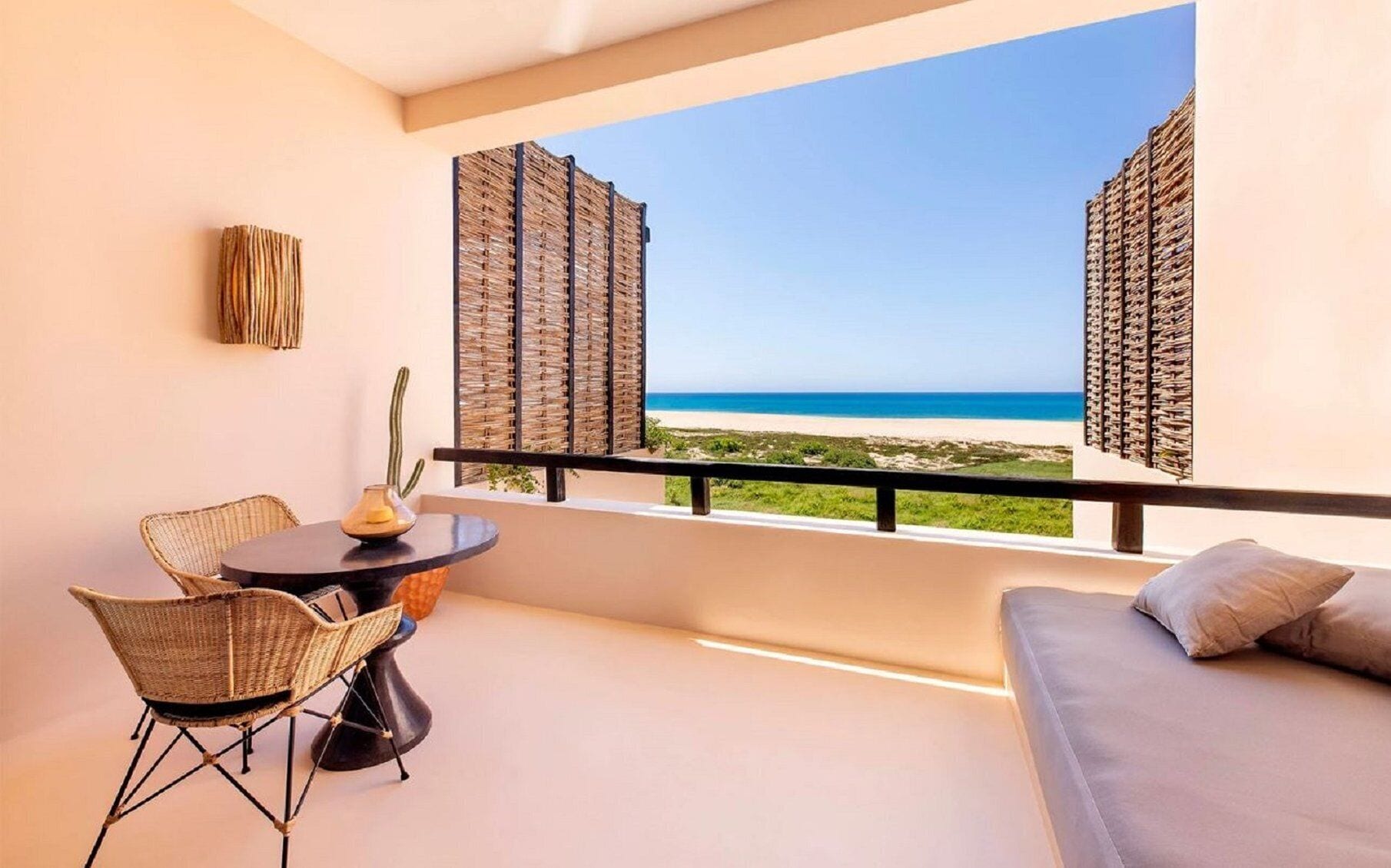 A balcony with a view of the beach, a table with chairs, and a sofa.