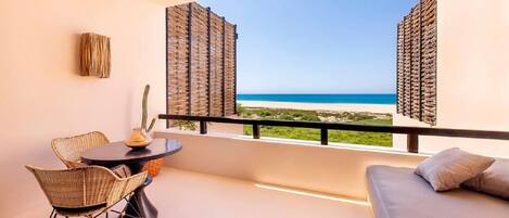 A balcony with a view of the beach, a table with chairs, and a sofa.