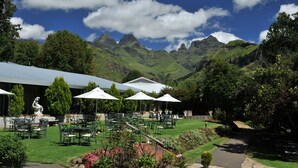 A patio area with outdoor seating and a statue, surrounded by lush greenery and mountains in the background.