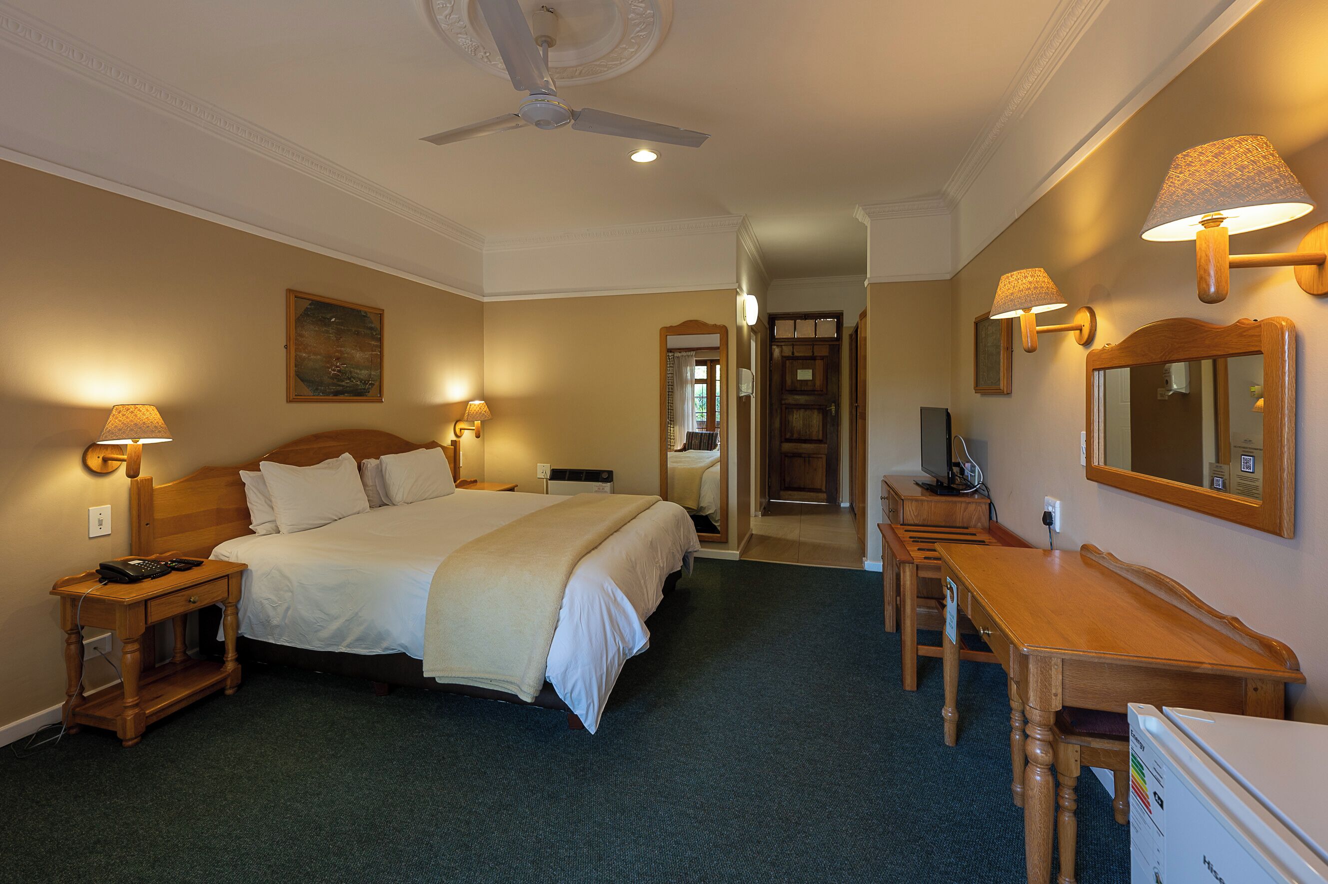 A hotel room with a bed, bedside table, lamp, desk, chair, and a ceiling fan.