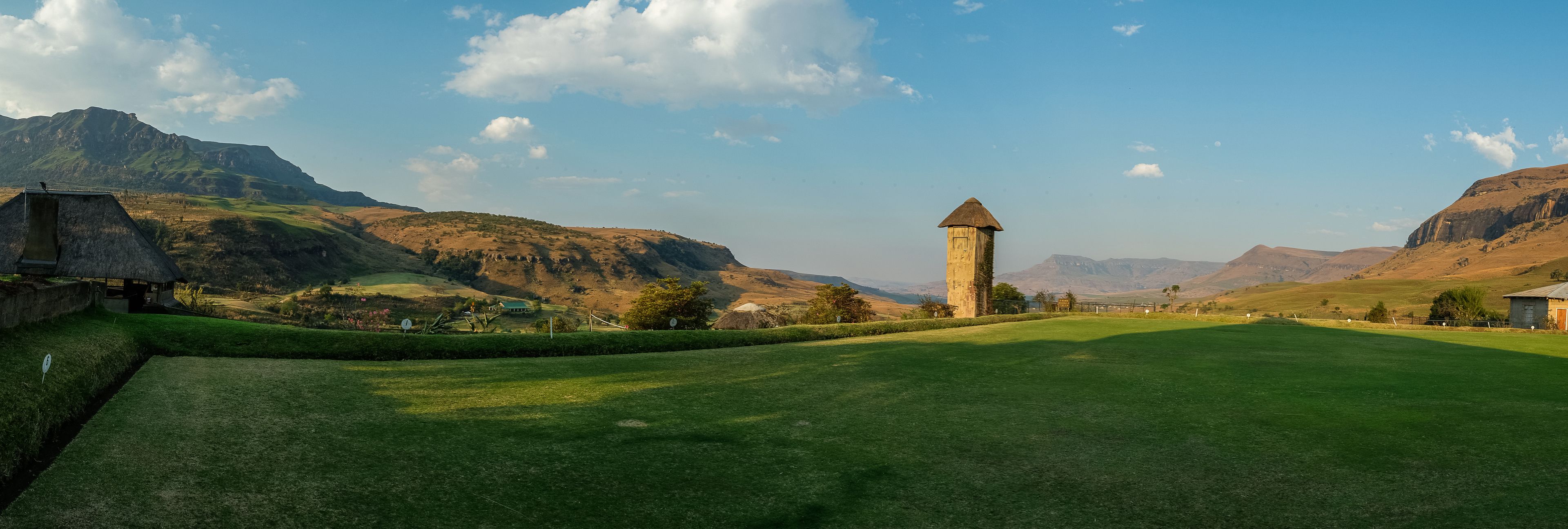 A golf course with a tower and thatched-roof buildings.