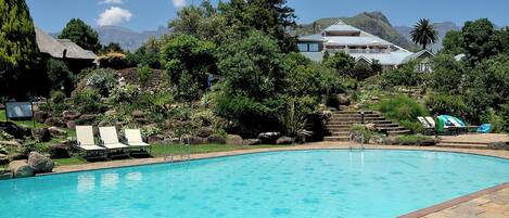 A swimming pool with lounge chairs, surrounded by greenery and mountains in the background.