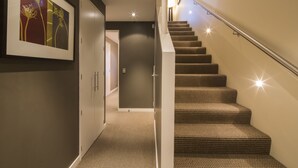 A staircase with a patterned carpet and a handrail, leading to a room with a door and a framed picture on the wall.