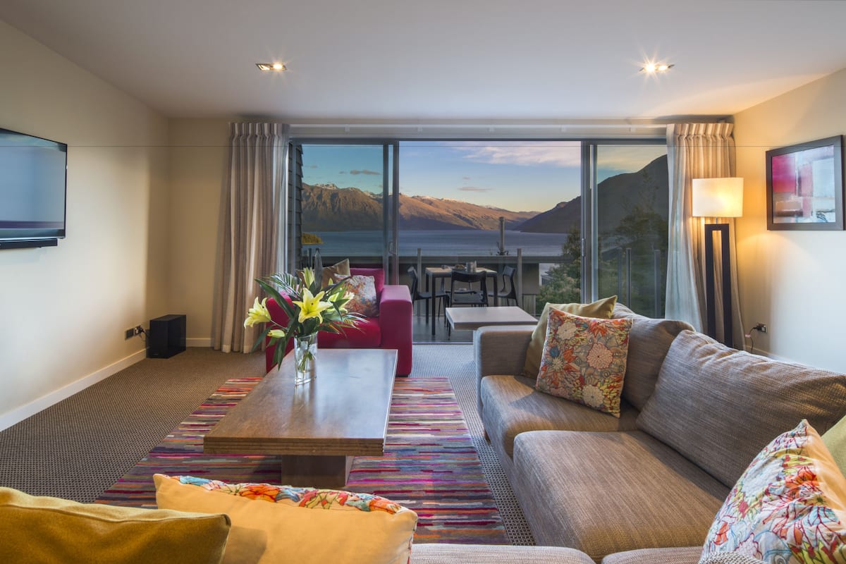 Una sala de estar moderna con un ventanal grande que ofrece una vista panorámica de montañas y un lago.