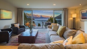 A modern living room with a large window offering a scenic mountain view. There is a sofa, a coffee table, and a chair.