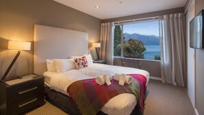 A hotel room with a large bed, a nightstand, a lamp, a view of the mountains and lake through the window.