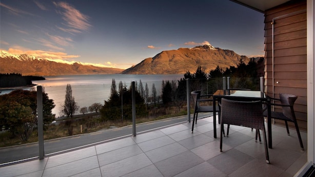 A balcony with a table and chairs overlooking a lake and mountains.