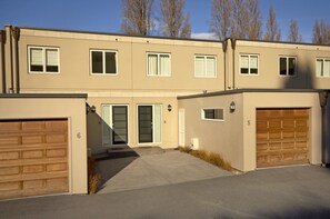 A two-story residential building with a beige exterior, two garage doors, and a front entrance with a door and steps.