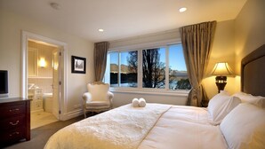 Une chambre d’hôtel avec un grand lit, une chaise, un bureau et une fenêtre donnant sur des arbres et des collines.