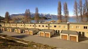 Une rangée de bâtiments à un seul étage, dotés de garages attenants, qui semblent être un motel ou une auberge, avec une vue sur des montagnes et un lac en arrière-plan.