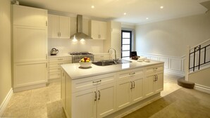 Une cuisine moderne avec des meubles blancs, un grand îlot central doté d’un évier et une hotte en acier inoxydable.