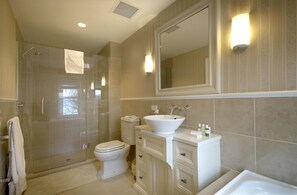 A modern bathroom with a glass-enclosed shower, a white toilet, a vanity with a sink, and a large mirror.