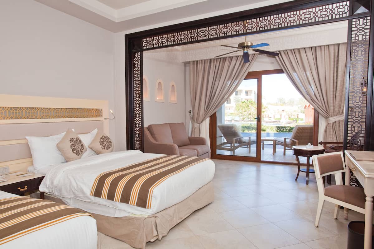 A hotel room with a large bed, a sofa, a dining table, and a view of the outdoor area.